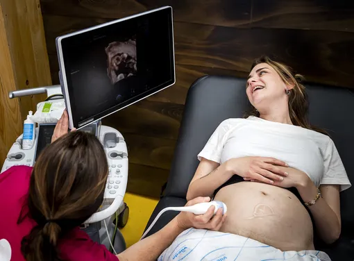 Беременная смотрит на экран во время УЗИ и улыбается