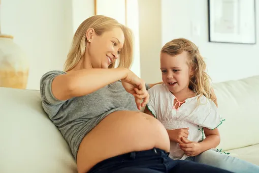 Беременная мама с дочкой топает пальцами по животу