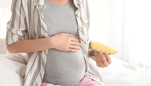 Беременная держит ананас и положила руку на живот