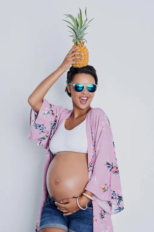 Беременная держит на голове ананас и смеется