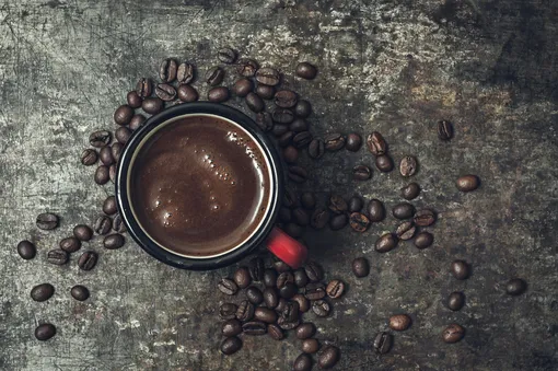 Черный кофе с пенкой в чашке и рассыпанные кофейные зерна
