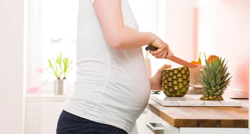 Беременная режет ананас на столешнице